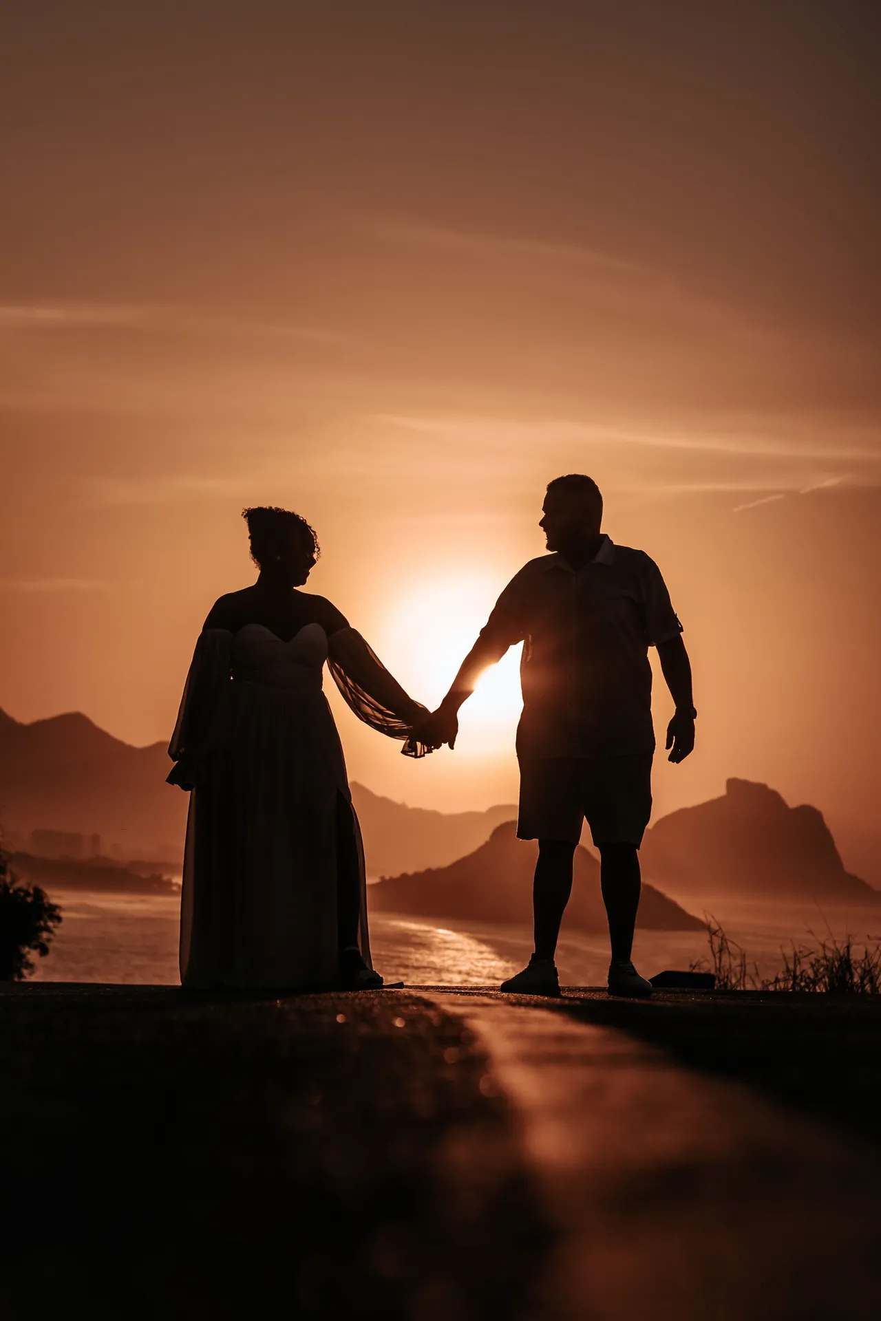 Silhueta de um casal de mãos dadas contra o sol se pondo sobre o mar