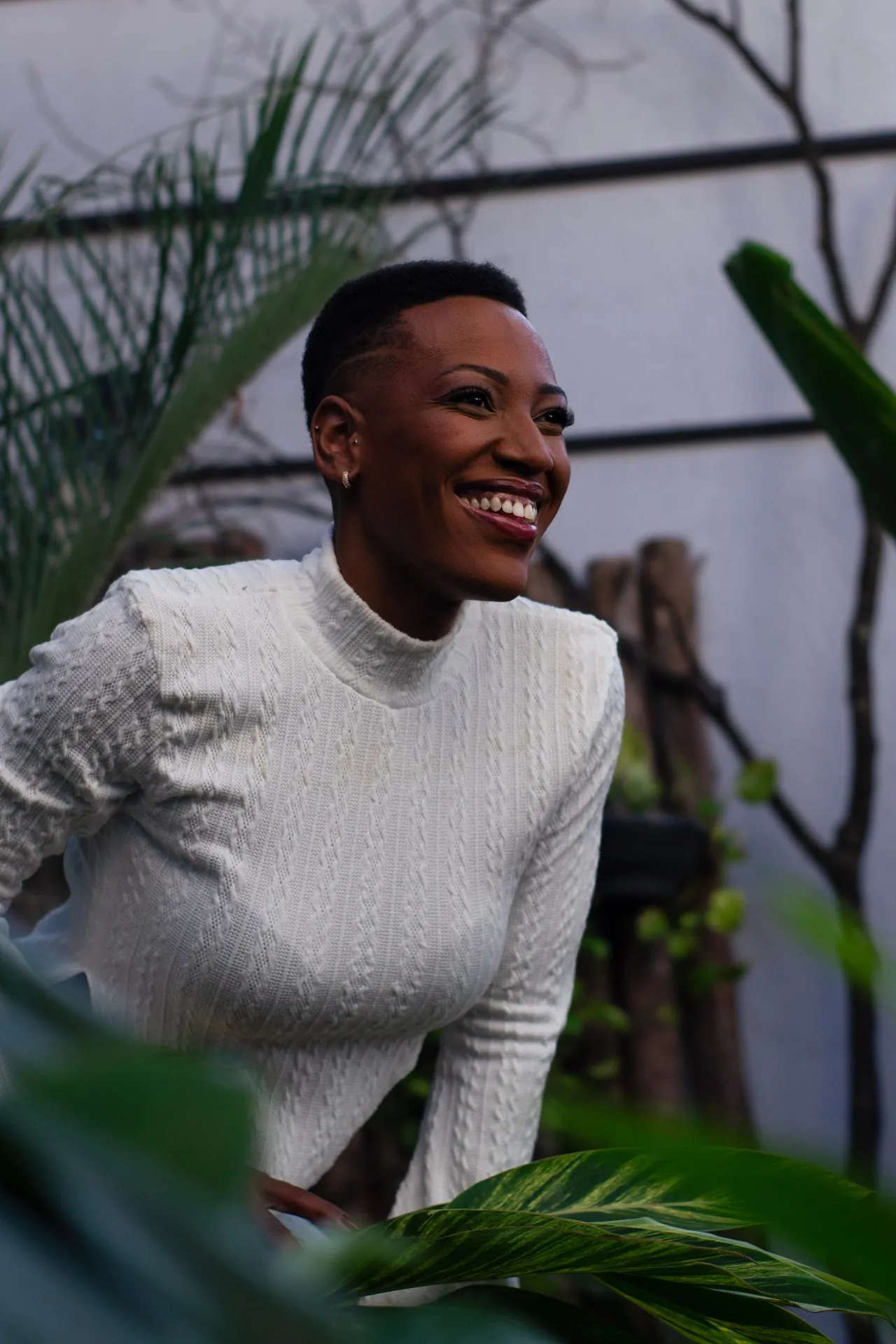 Mulher sorrindo ao ar livre, com folhagem desfocada ao fundo