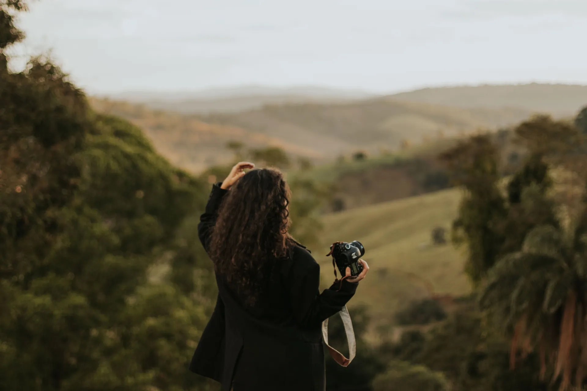 Fotógrafa com a câmera na mão observando um vale verde