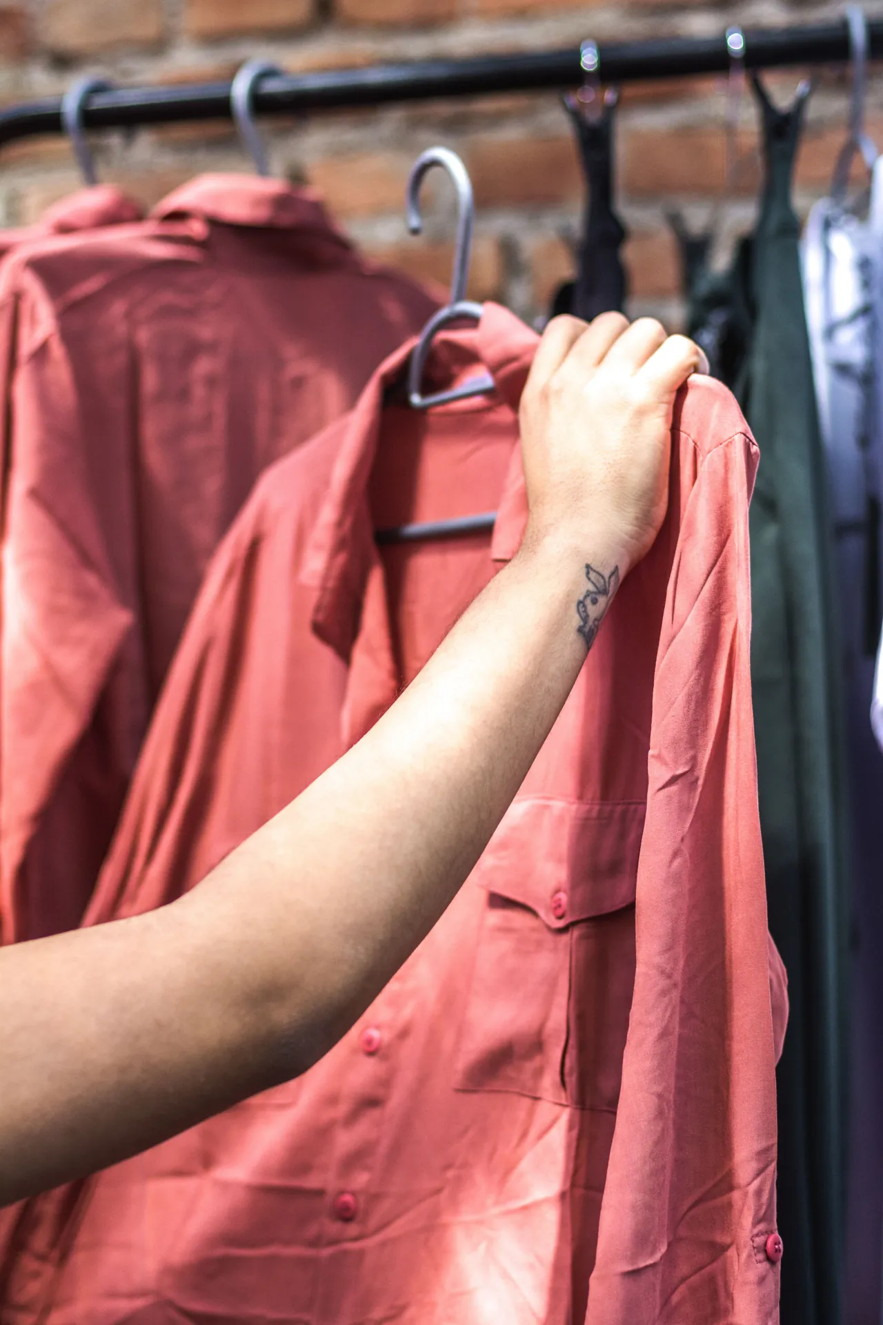 Mão escolhendo uma camisa entre várias peças penduradas numa arara