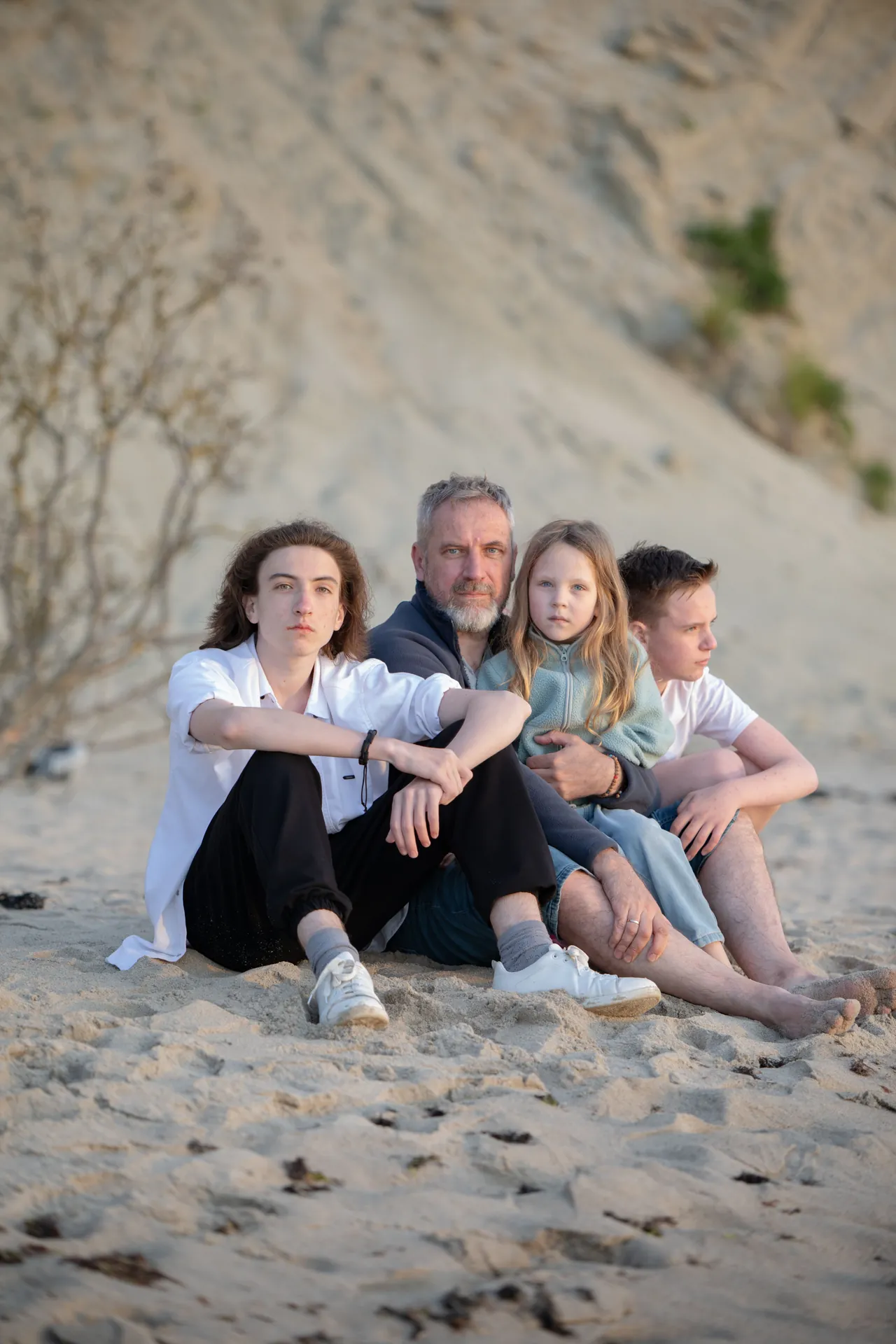 Família sentada na areia da praia, encostada numa duna