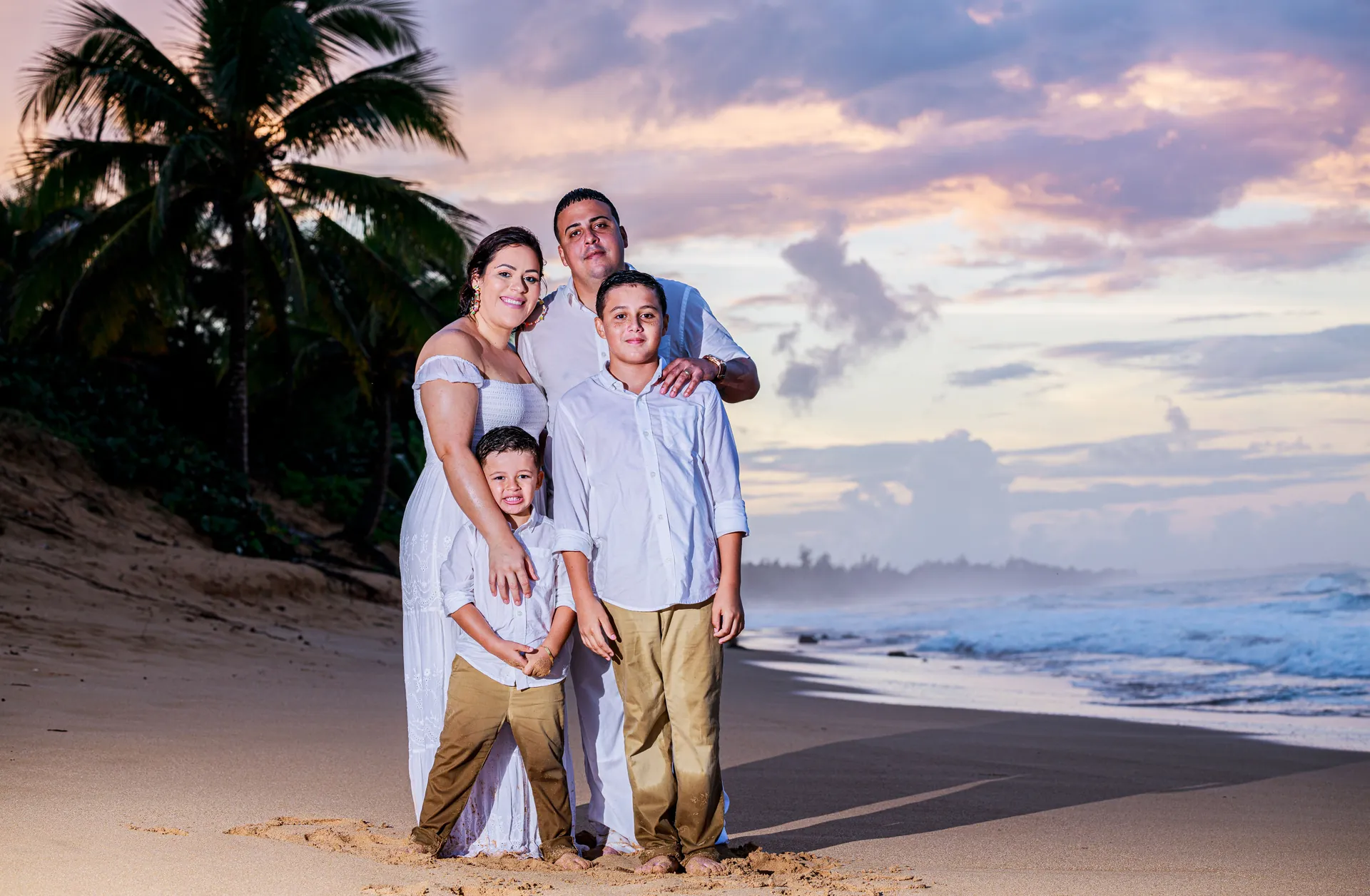 Família de quatro em roupas claras na praia, ao pôr do sol