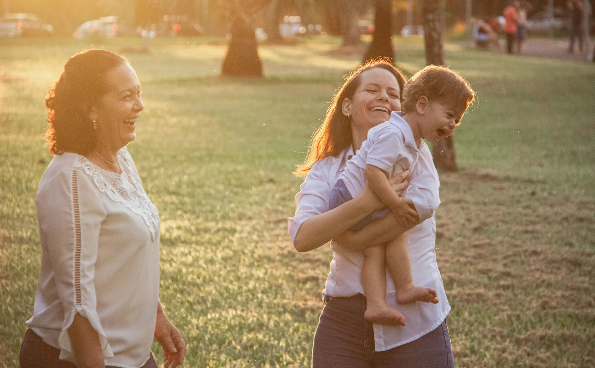 Mulher rindo com uma criança pequena no colo, num parque com luz dourada