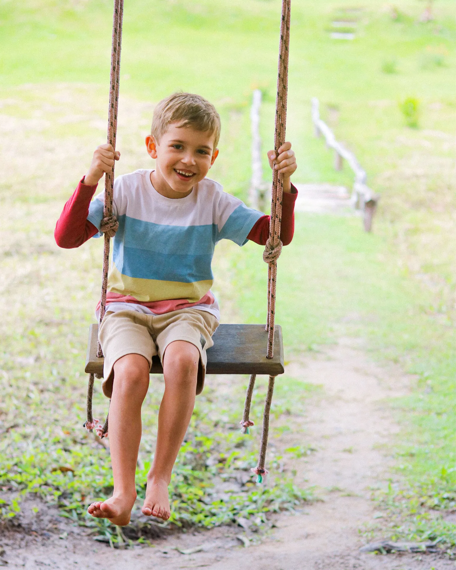 Menino sorrindo num balanço de corda, num caminho de grama