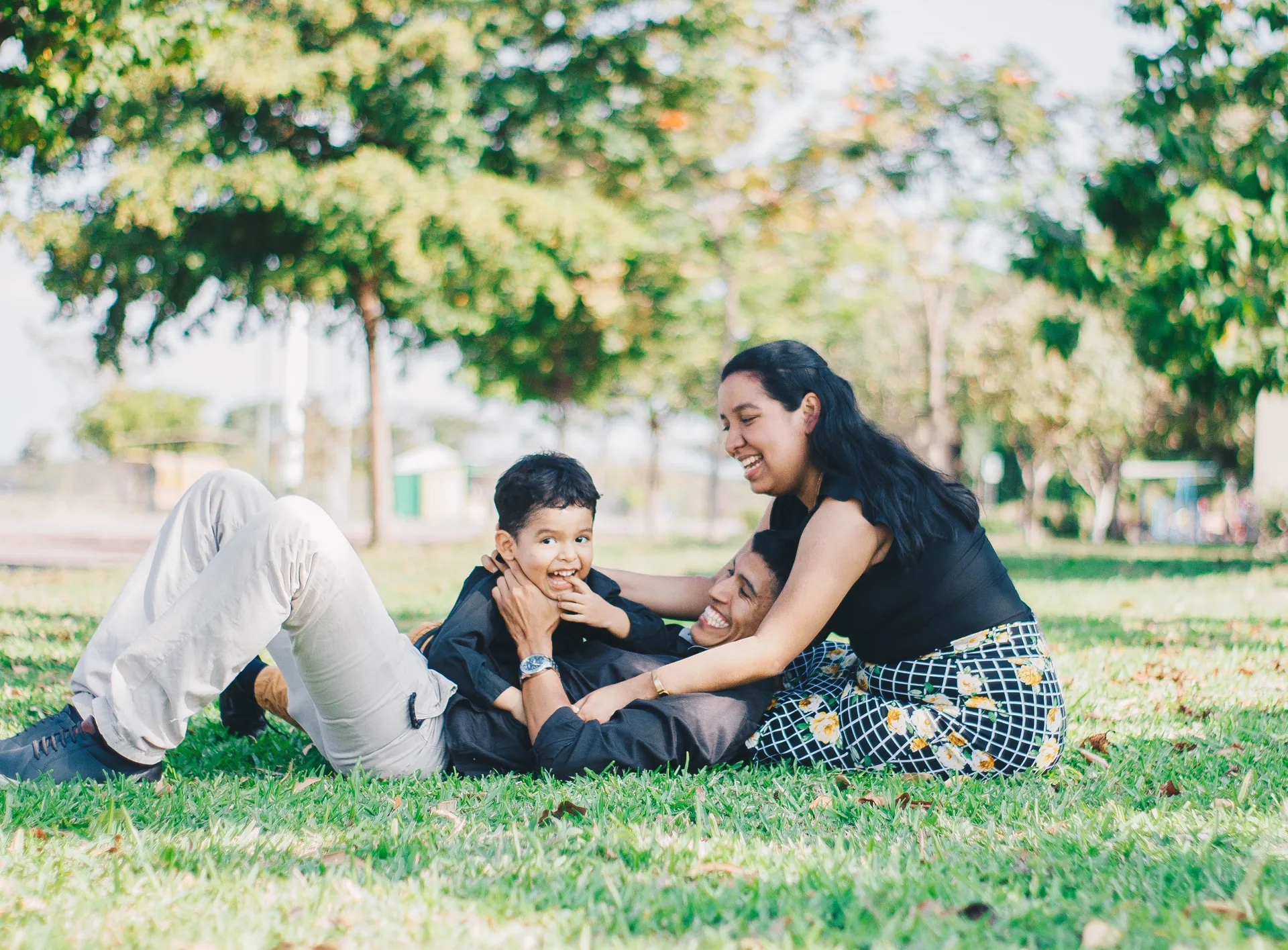 Pai, mãe e filho deitados na grama, rindo juntos