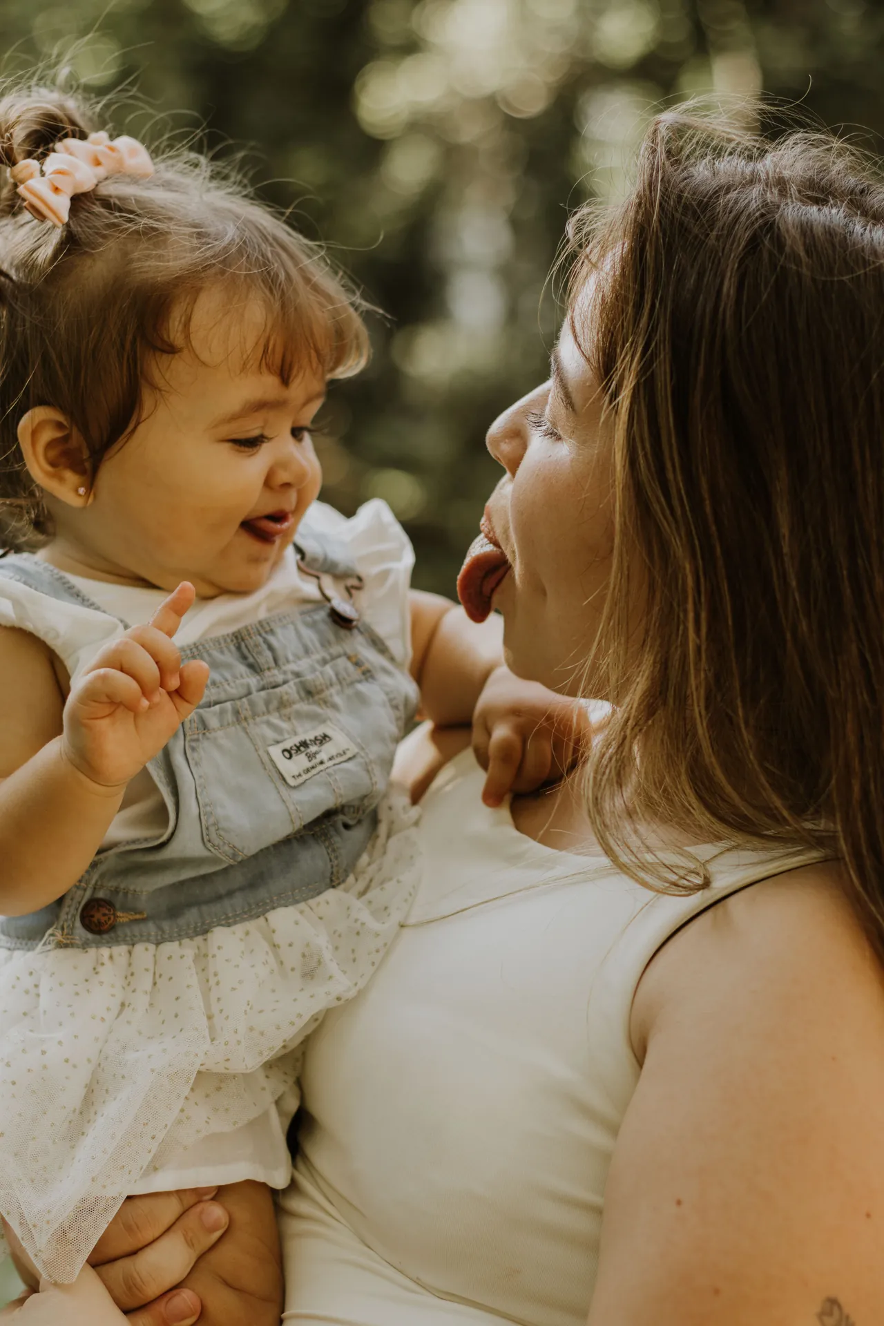 Mãe e filho pequeno mostrando a língua um pro outro, com o verde do parque desfocado