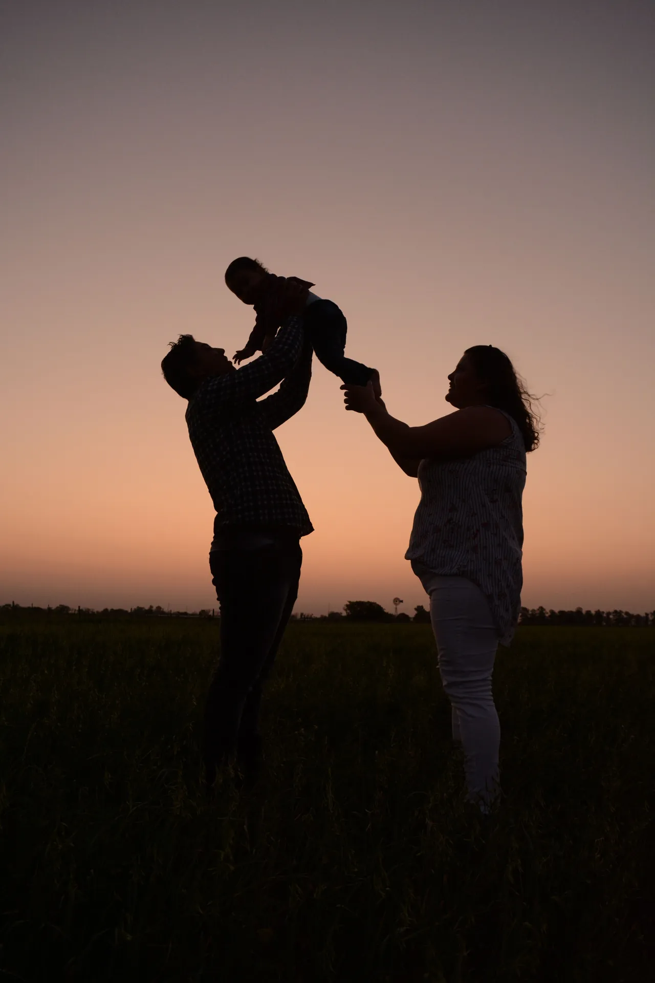 Silhueta dos pais erguendo o bebê entre eles no pôr do sol
