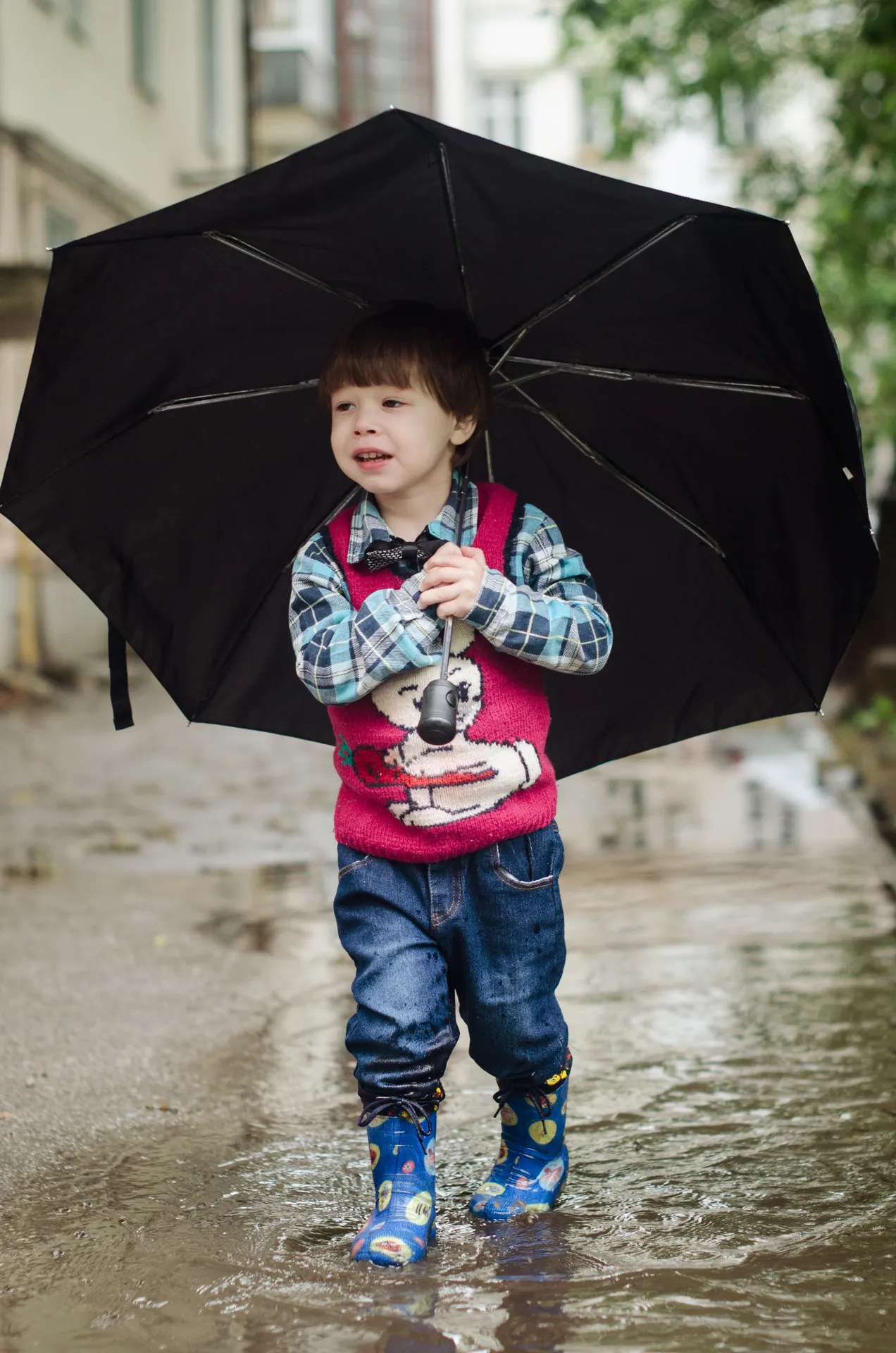 Menino de galocha e guarda-chuva pisando numa poça, num dia de chuva