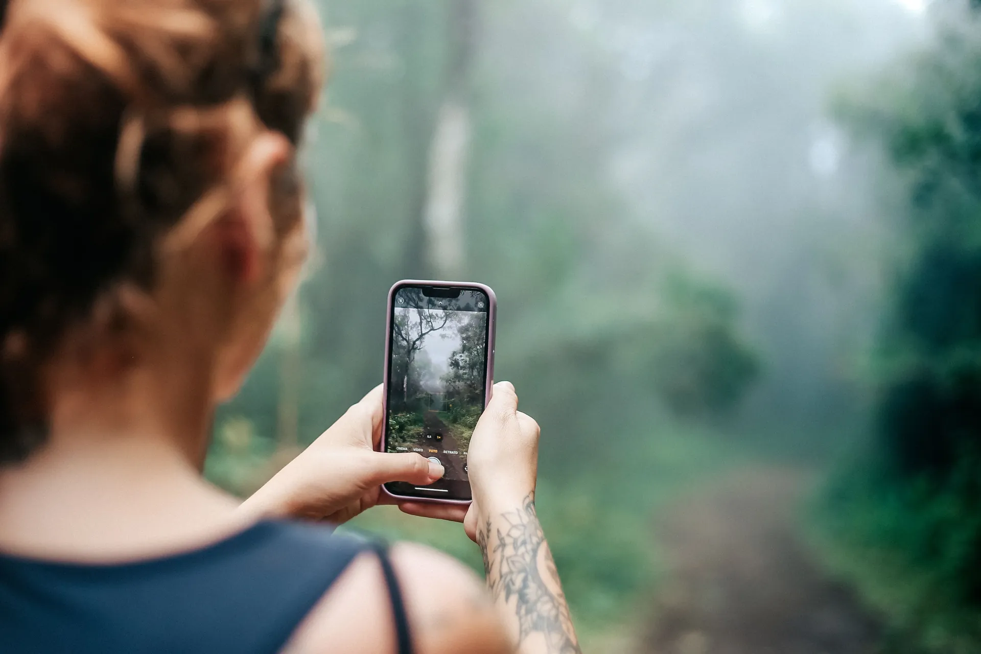 Mulher fotografando uma trilha de mata com o celular