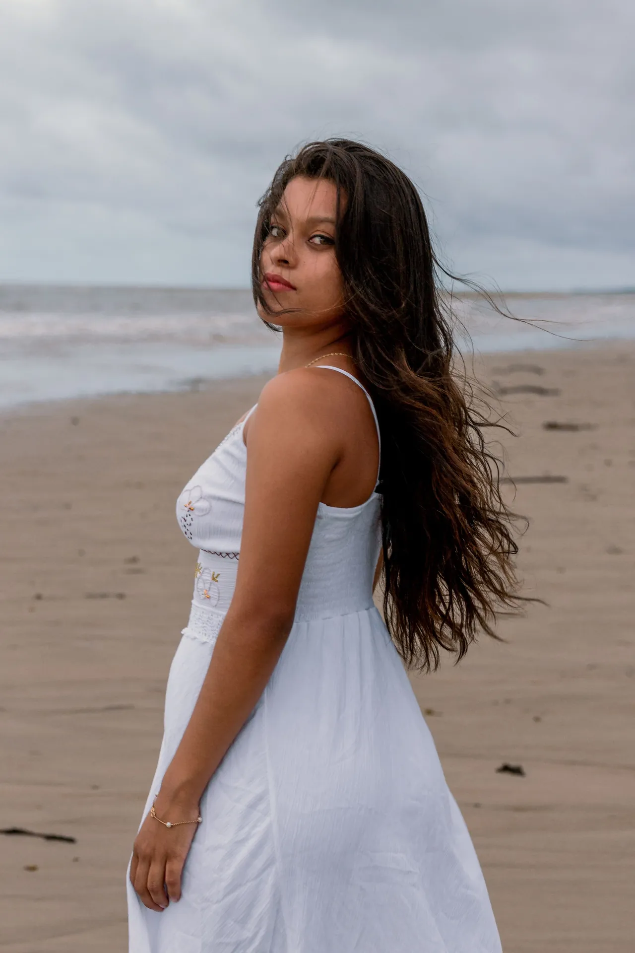 Mulher de vestido branco na praia, com o cabelo solto ao vento