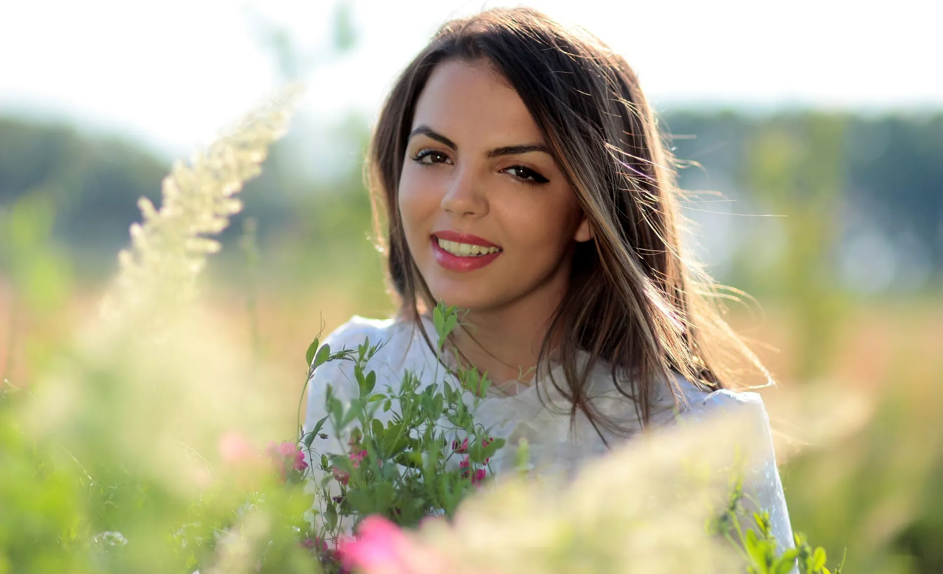 Mulher sorrindo em meio a flores do campo, na luz dourada