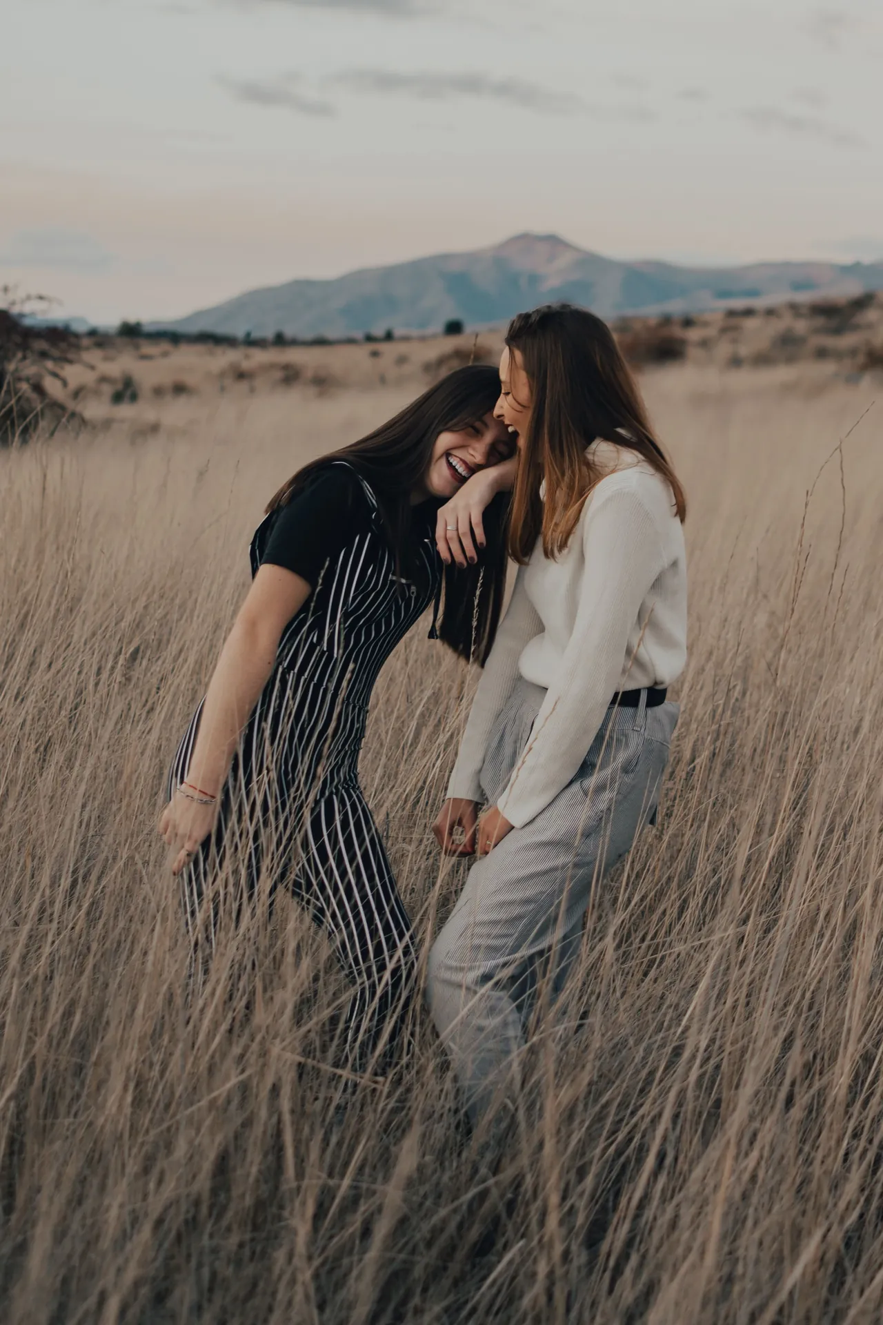 Duas amigas rindo juntas num campo de capim alto