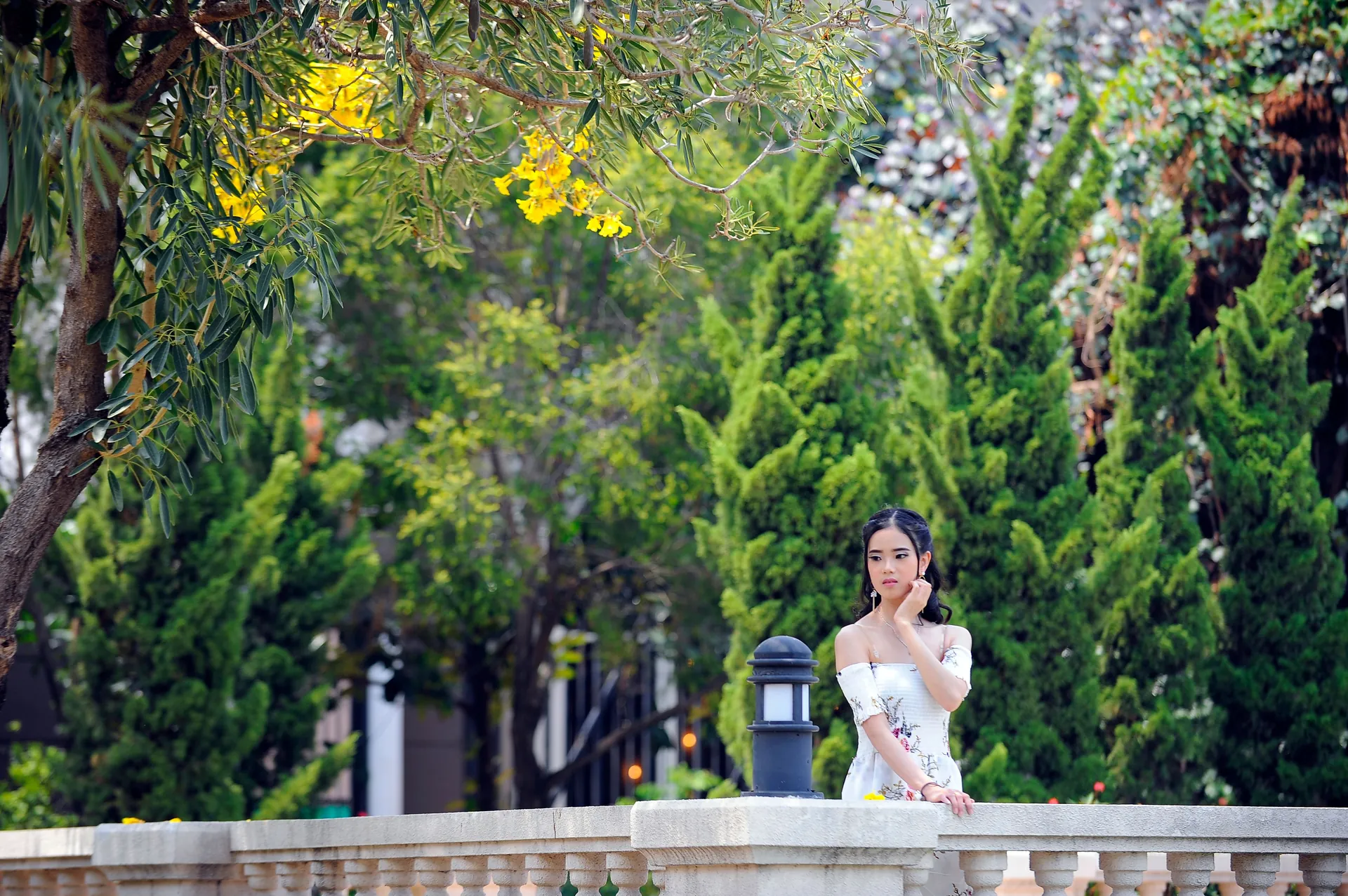 Mulher de vestido florido posando apoiada numa balaustrada de jardim