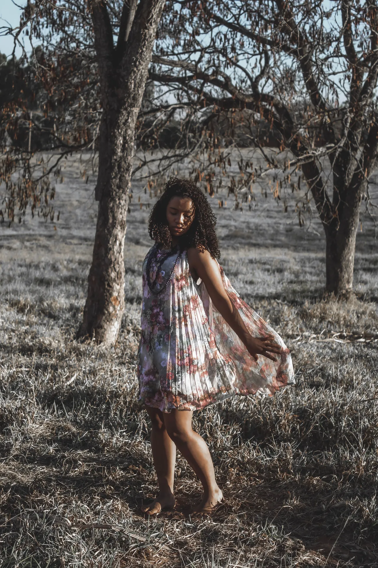 Mulher de vestido florido rodado caminhando num campo seco
