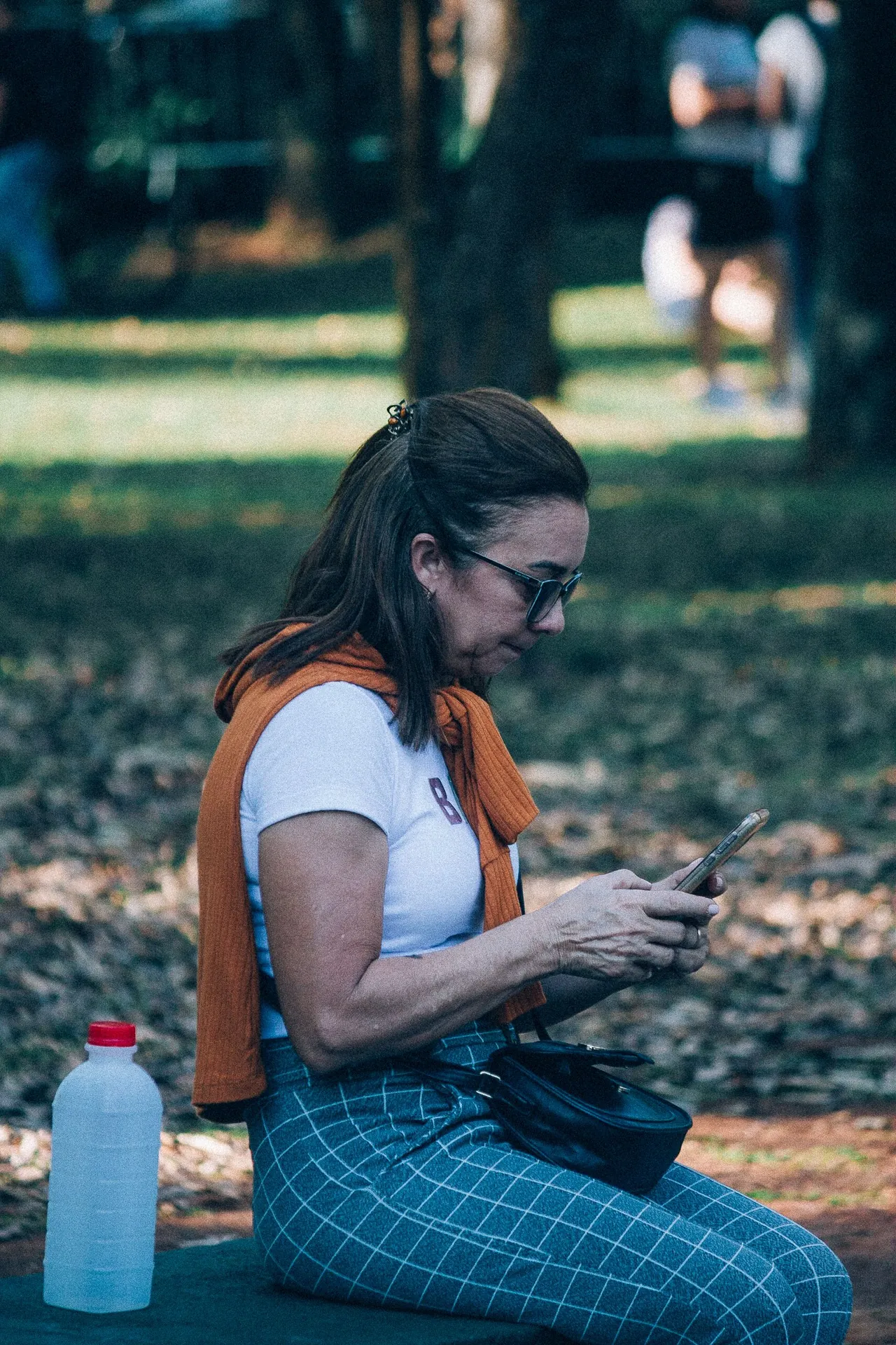 Mulher sentada num banco de parque olhando as fotos no celular