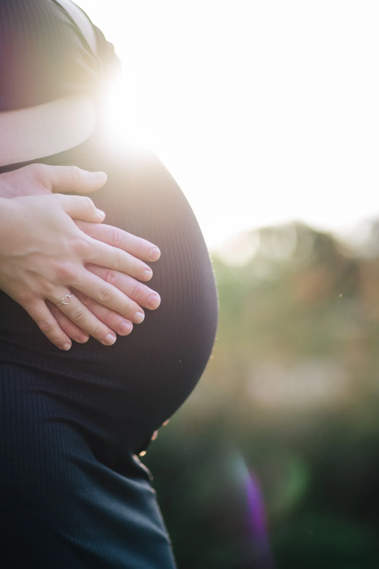 Mãos do casal sobre a barriga da gestante, em contraluz dourado