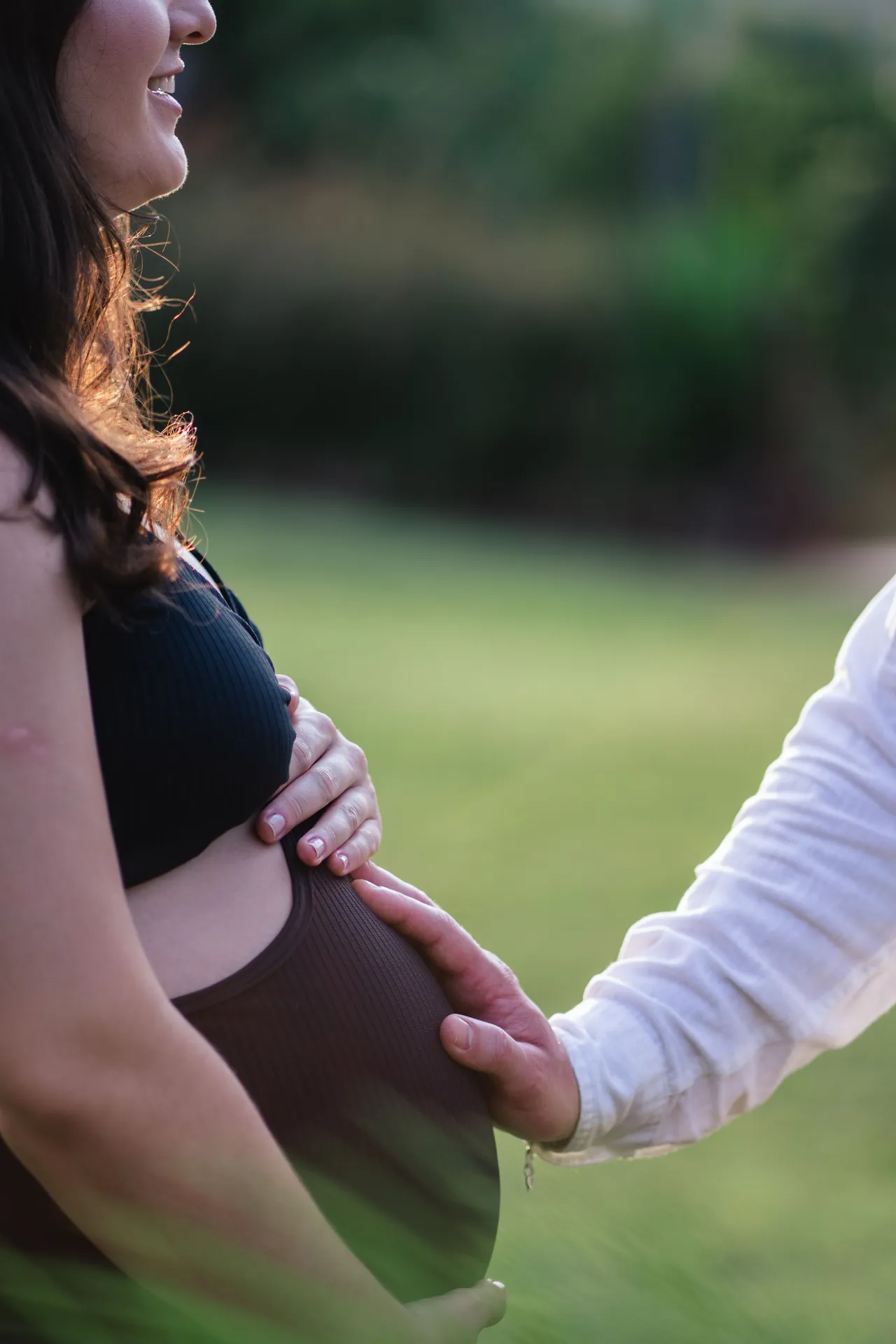 Mão do companheiro apoiada na barriga da gestante, com fundo verde desfocado