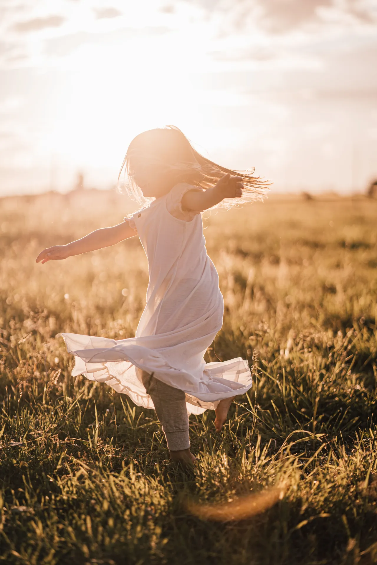 Menina rodopiando de vestido claro num campo dourado ao fim da tarde