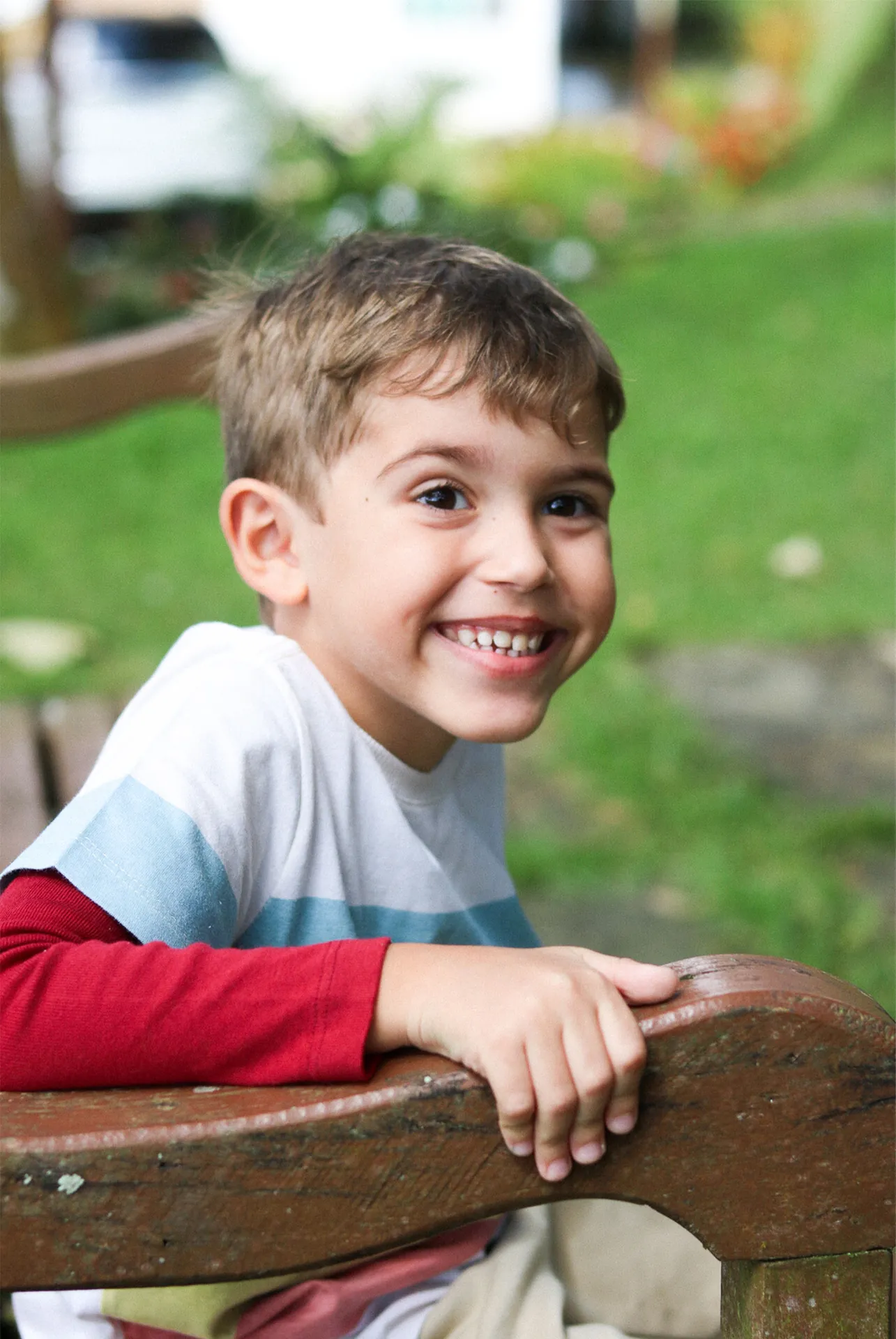 Menino sorrindo de perto, com o verde do parque desfocado atrás
