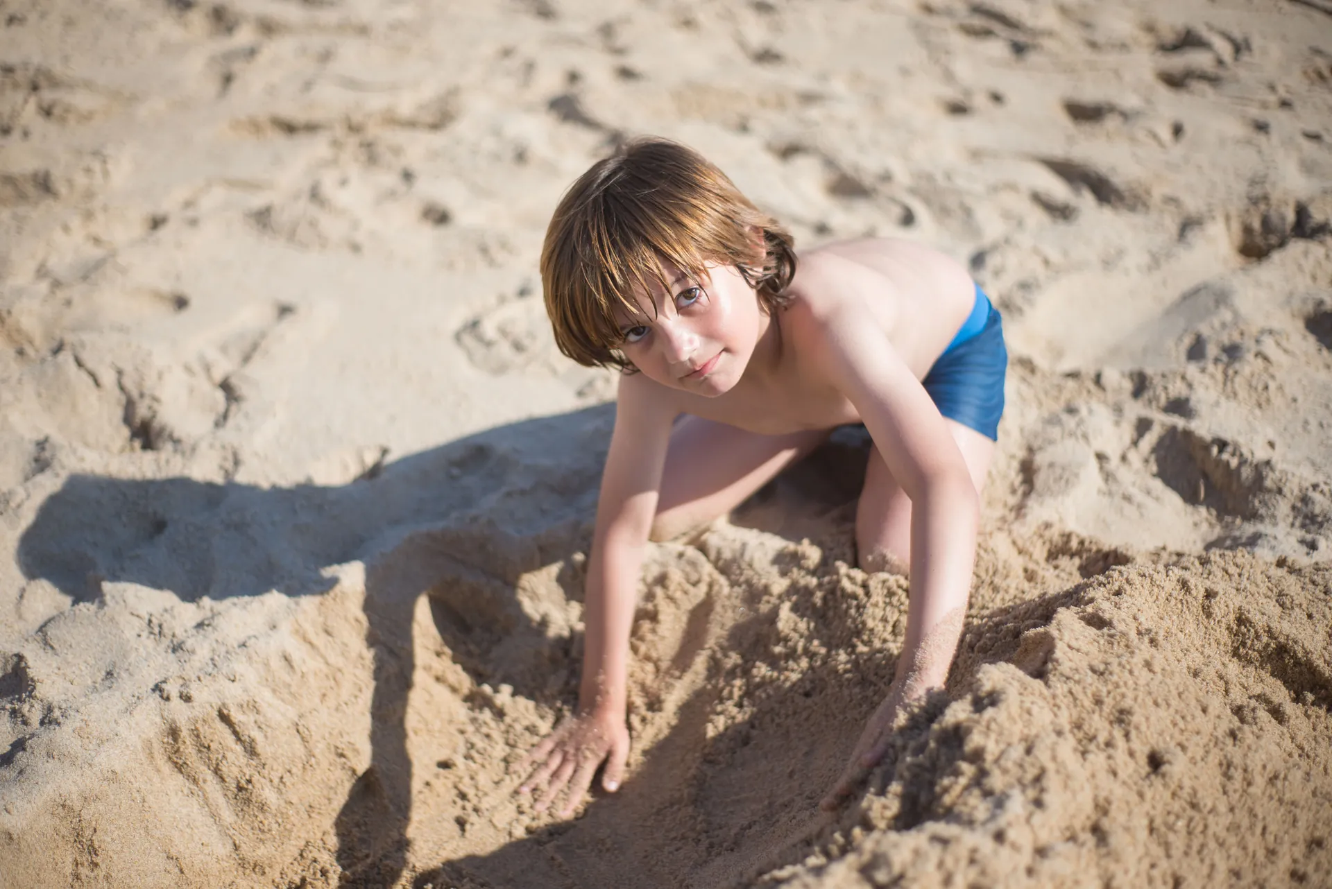 Menino brincando na areia, cavando com as mãos