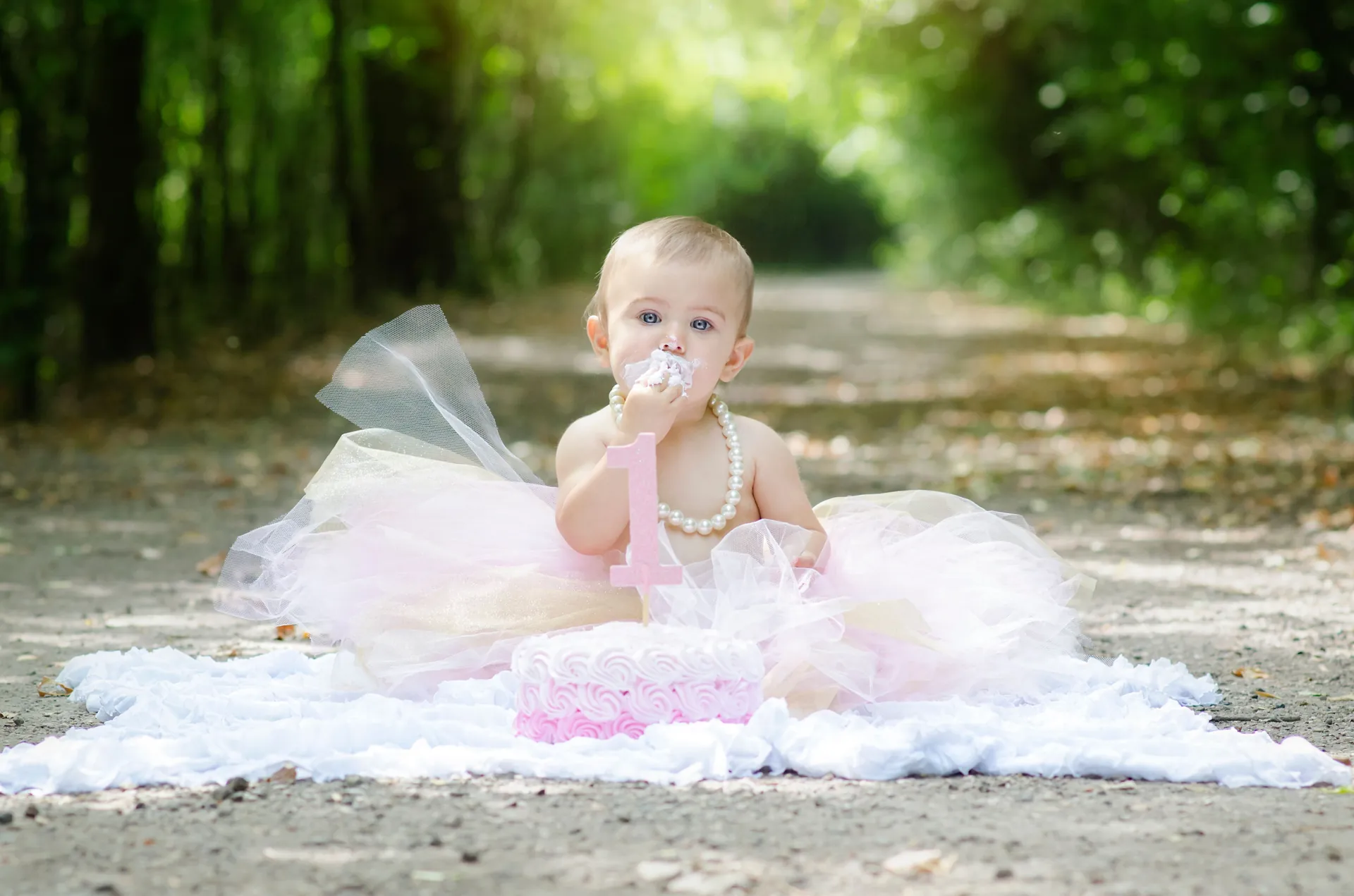 Bebê de tutu rosa com colar de pérolas provando o bolo de smash the cake numa trilha