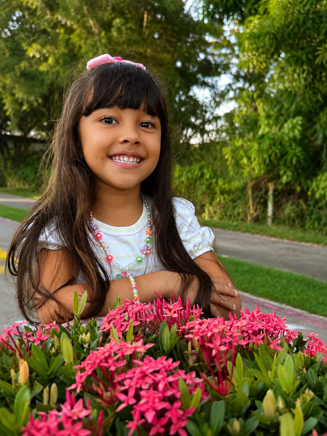 Maria Lívia sorrindo apoiada num canteiro de flores vermelhas na Praia do Paiva