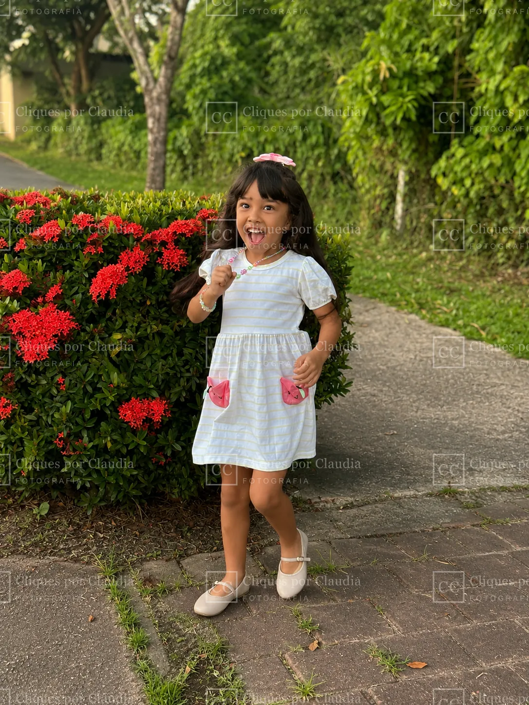 Menina de vestido listrado rindo ao lado de um canteiro de flores vermelhas no Paiva
